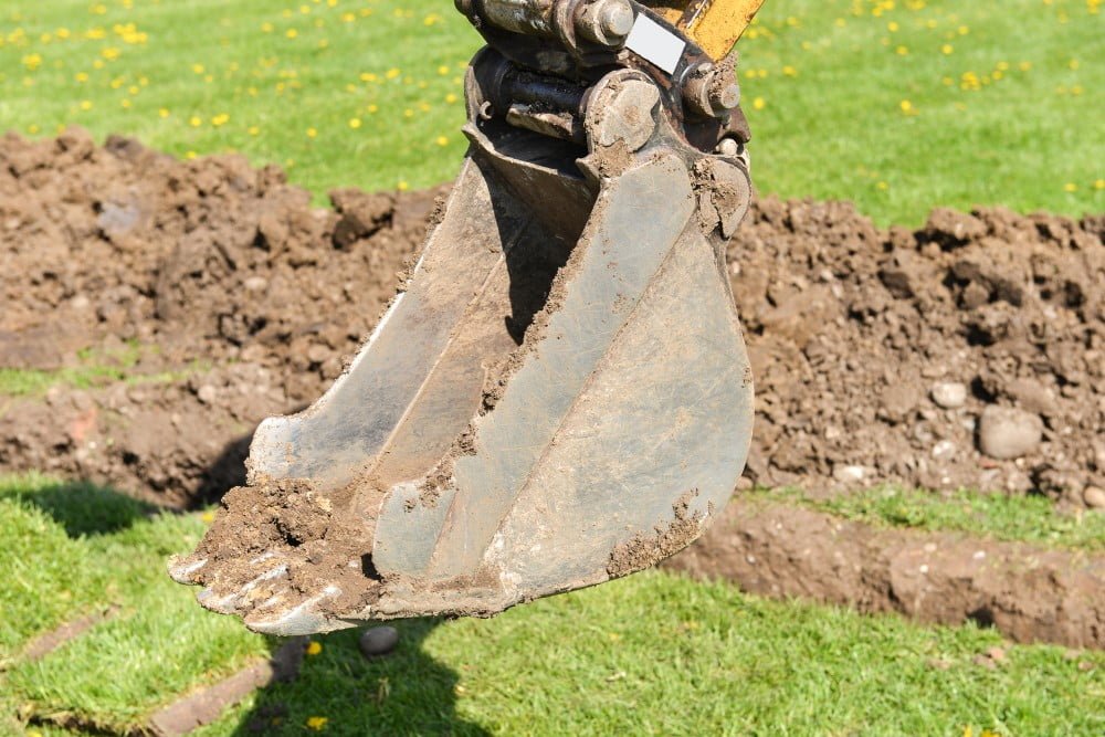 Entreprenør der graver en rende i en have med en gravemaskine